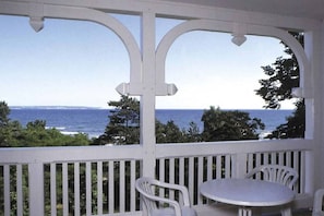 Un espace extérieur abrité, avec vue sur la mer, doté de rampes blanches et d’une table ronde entourée de chaises.