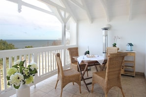 A covered patio with wicker chairs, a table with a white tablecloth, a bottle of wine, and a small house model. - Directly on the beach promenade, balcony with sea view - Aparthotel Ostsee FeWo 35 (Binz)