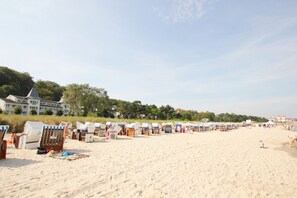 Une plage bordée de rangées de chaises longues et de parasols, un grand bâtiment en arrière-plan et un ciel dégagé.