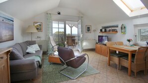 A spacious living area with a sofa, armchair, dining table, and a TV.