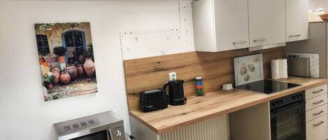 A compact kitchen with a microwave, stove, and a small sink. There's a wooden countertop, a white cabinet, and a picture of pots on the wall.