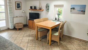 A cozy living room with a wooden dining table, wicker chairs, a television, and a skylight.