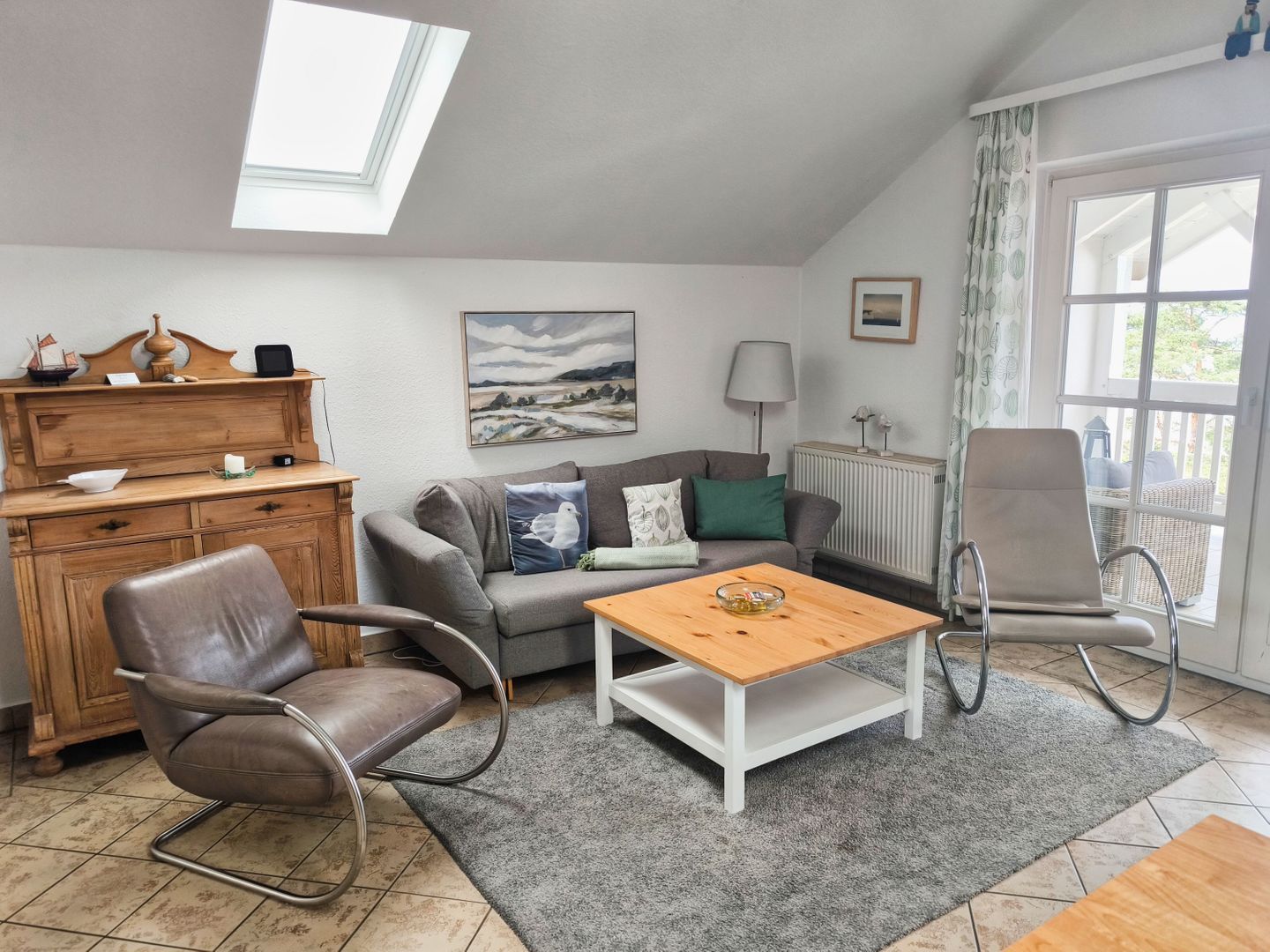 Een gezellige woonkamer met een bank, twee fauteuils, een houten bijzettafeltje, een open haard en een groot raam.