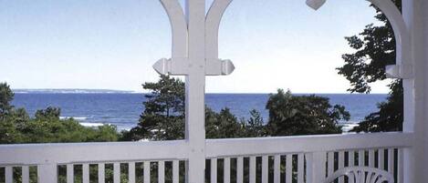 Un espacio al aire libre cubierto con vistas al mar, barandillas blancas y una mesa redonda con sillas.