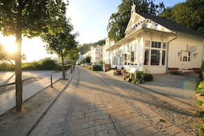 A building with a sign reading "Strandhalle" and a paved street with trees and benches. - Directly on the beach promenade, balcony with sea view - Aparthotel Ostsee FeWo 10 (Binz)
