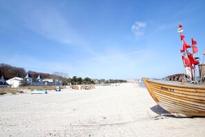 A sandy beach with a wooden boat named BIN-11, a row of beach huts, and a building with a blue roof in the background. - Directly on the beach promenade, balcony with sea view - Aparthotel Ostsee FeWo 10 (Binz)