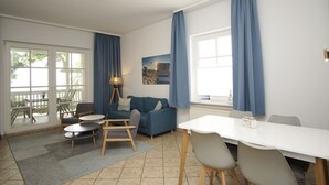 Un salon moderne avec un canapé, des fauteuils, une table à manger et une grande fenêtre agrémentée de rideaux.