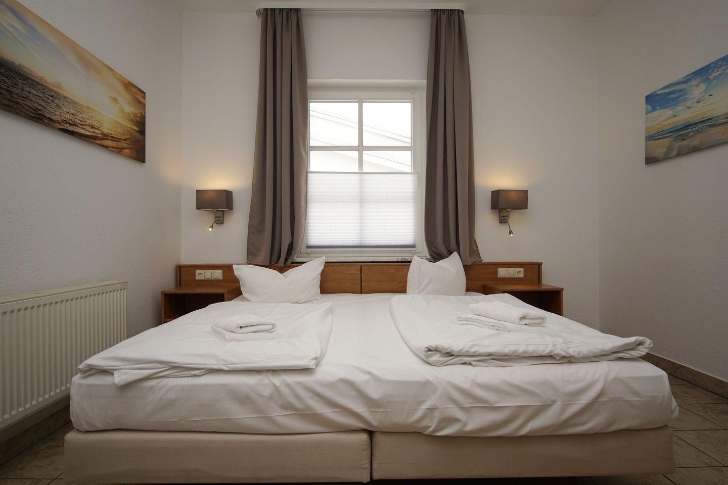 Une chambre d’hôtel avec un grand lit, deux tables de chevet, une fenêtre avec des rideaux et des lampes fixées au mur.