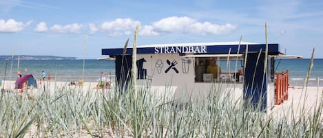Una chiosco gastronomico sulla spiaggia chiamato STRANDBAR, con vista diretta sul mare e sulla spiaggia.