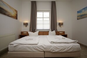 Habitación de hotel con una cama grande, dos mesitas de noche, una ventana con cortinas y lámparas fijadas a la pared.