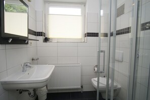 Een moderne badkamer met een wit wastafelmeubel, toilet en een douchecabine van glas.