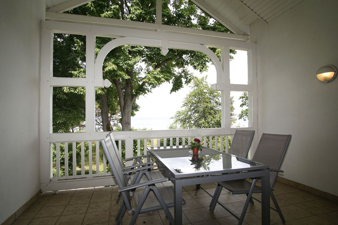 A covered patio with a table and chairs, a potted plant, and a view of trees and sky.