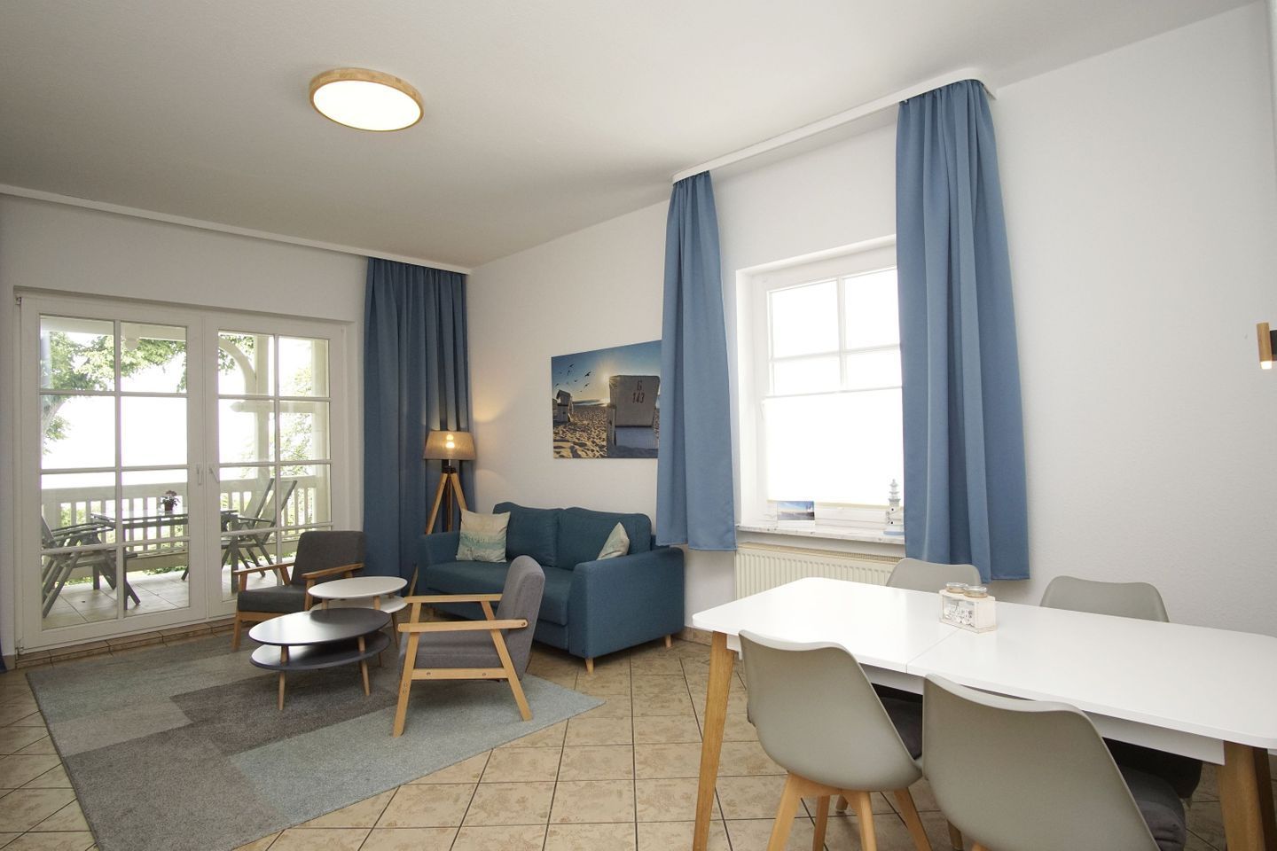 A modern living room with a sofa, chairs, a dining table, and a large window with curtains.