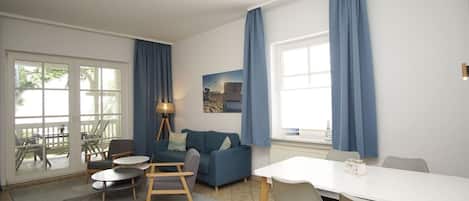 Una sala de estar moderna con un sofá, sillas, una mesa de comedor y un ventanal con cortinas.