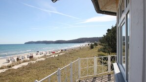 A beach view from a balcony with a railing, a pier in the distance, and a grassy area with beach chairs.