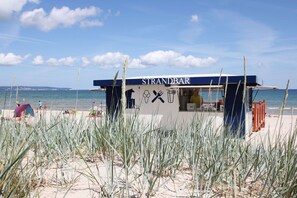 Ein Küstenimbiss namens STRANDBAR mit freiem Blick auf das Meer und den Strand im Hintergrund.