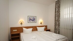 A hotel room with a double bed, two bedside lamps, a painting on the wall, and a window with curtains.