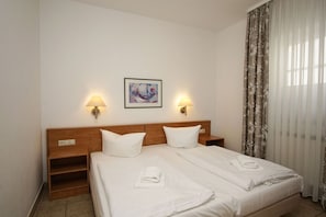 A hotel room with a double bed, two bedside lamps, a painting on the wall, and a window with curtains.