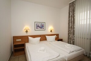 A hotel room with a double bed, two bedside lamps, a painting on the wall, and a window with curtains. - Right on the beach promenade, balcony with a view of the sea - Aparthotel Ostsee FeWo 06 (Binz)