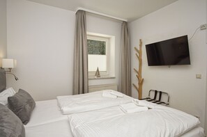 Une chambre d’hôtel avec un lit, une télévision, une fenêtre avec des rideaux et un porte-manteau.
