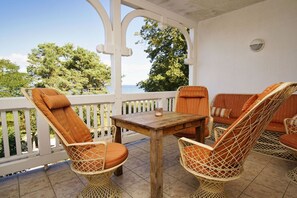 A covered outdoor seating area with wicker chairs and a wooden table, overlooking a scenic view.