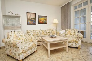 Un salon avec des canapés à motifs floraux, une table basse en bois et deux tableaux encadrés accrochés au mur.
