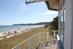 A beach view from a balcony with a railing, a pier in the distance, and a grassy area with beach chairs.