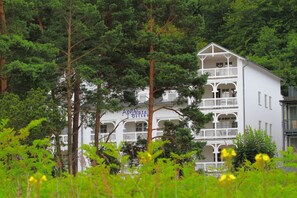 Un immeuble blanc à plusieurs étages, doté de balcons, entouré d’arbres verdoyants et luxuriants.