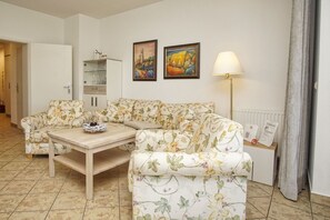 Un salon avec un canapé à motifs floraux, une table basse en bois, un lampadaire et deux tableaux encadrés accrochés au mur.
