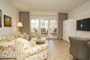 A living room with a floral sofa, a coffee table, and a TV mounted on the wall. - Directly on the beach promenade, balcony with sea view - Aparthotel Ostsee FeWo 15 (Binz)