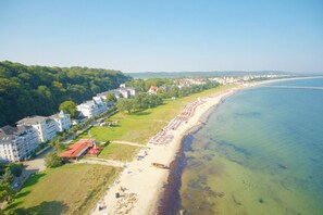 An aerial view of a coastal area with a beach, buildings, and a forested hillside.