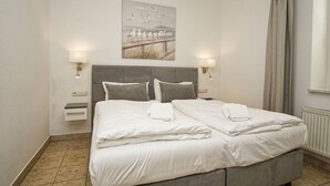 A double bed with white linens, two bedside tables, wall-mounted lamps, and a painting of seagulls on the wall. - Directly on the beach promenade, balcony with sea view - Aparthotel Ostsee FeWo 15 (Binz)