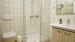 Een moderne badkamer met een douchecabine van glas, een wit toilet, een wastafel met spiegel en een kleine prullenbak.