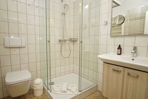 Une salle de bain moderne avec une douche en verre, des toilettes blanches, un lavabo avec un miroir et une petite poubelle.