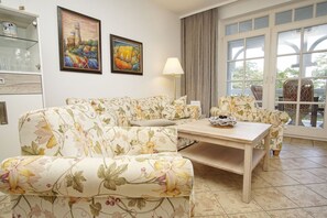 A living room with floral upholstery, a glass cabinet, and two paintings. - Right on the beach promenade, balcony with a view of the sea - Aparthotel Ostsee FeWo 15 (Binz)