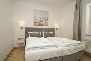 A double bed with white linens, two bedside tables, wall-mounted lamps, and a painting of seagulls on the wall. - Directly on the beach promenade, balcony with sea view - Aparthotel Ostsee FeWo 15 (Binz)