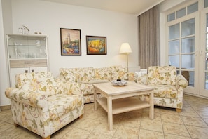A living room with floral-patterned sofas, a wooden coffee table, and two framed paintings on the wall. - Right on the beach promenade, balcony with a view of the sea - Aparthotel Ostsee FeWo 15 (Binz)
