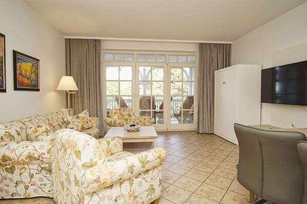 A living room with a floral sofa, a coffee table, and a TV mounted on the wall.