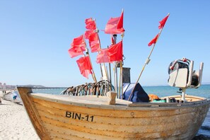 Un bateau en bois portant le numéro d’identification BIN-11 était amarré sur une plage où flottaient des drapeaux rouges, et il y avait un moteur sur le pont.
