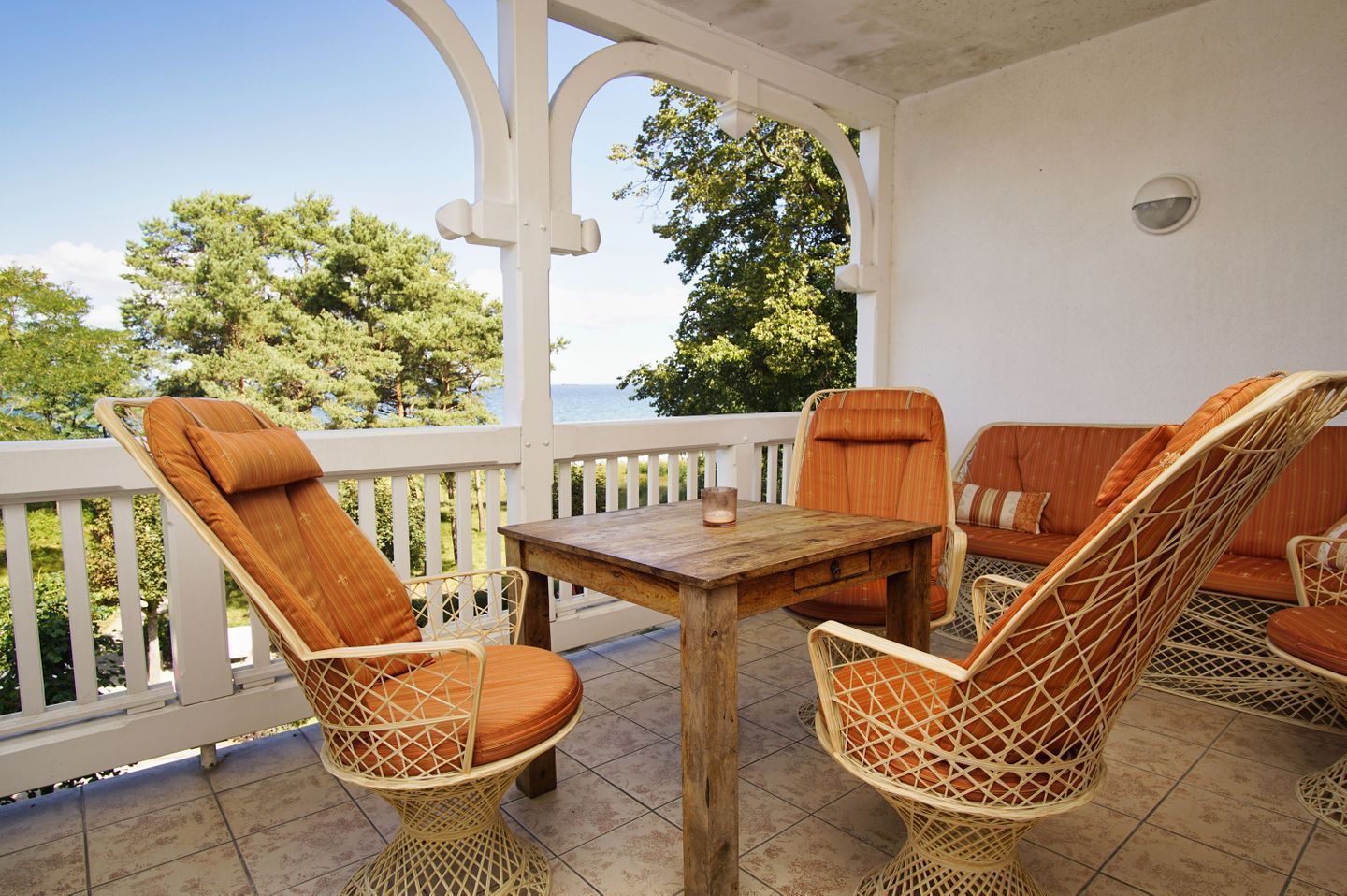 A covered outdoor seating area with wicker chairs and a wooden table, overlooking a scenic view.