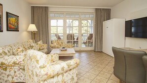 A living room with a floral sofa, a coffee table, and a TV mounted on the wall. - Directly on the beach promenade, balcony with sea view - Aparthotel Ostsee FeWo 15 (Binz)