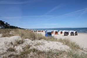 A beach with row of beach huts and a sandy area with grass in the foreground.