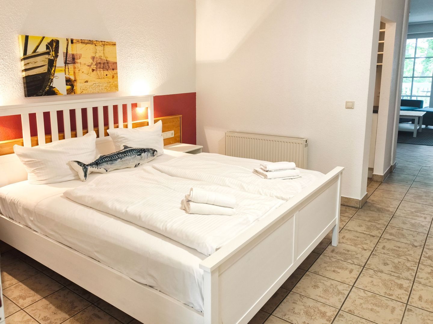 A neatly made bed with white linens and a decorative pillow, a white headboard, and a wall-mounted artwork.