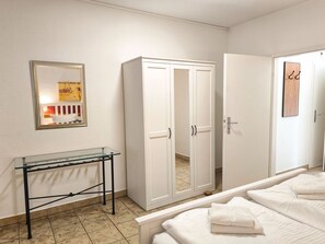 A bedroom with a bed, a wardrobe, a glass table, and a door. - Directly on the beach promenade, balcony with sea view - Aparthotel Ostsee FeWo 26 (Binz)