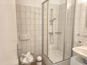 A modern bathroom with a glass-enclosed shower, a toilet with a towel rack, and a sink.