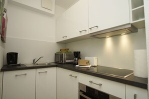 Una cucina moderna con mobili bianchi, un lavello in acciaio inossidabile, un forno a microonde e una macchina da caffè.