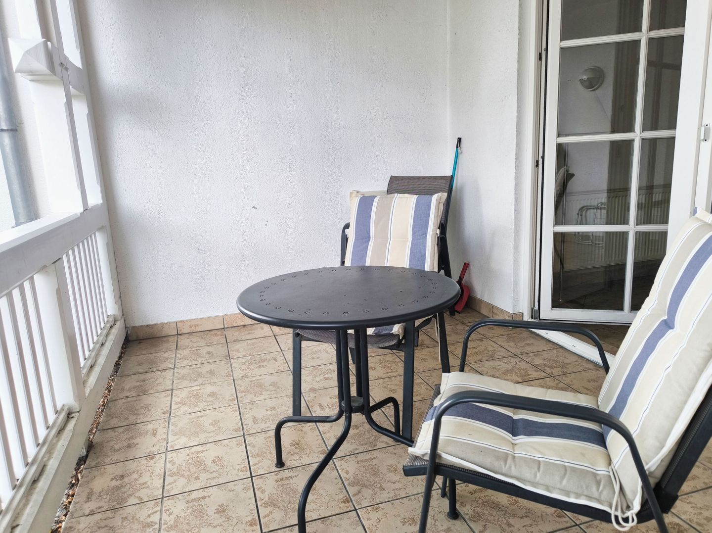 A small patio area with a round table and two chairs, a white railing, and a sliding glass door.