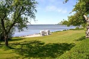A grassy area with a white outdoor seating area and a view of a lake. - A Seaside Getaway, Private Swimming Area - Gutshof Ostseeblick FeWo 01 - (Putbus)