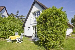 A white house with a balcony, surrounded by lush greenery and a small lawn with a yellow table and chairs. - A Seaside Getaway, Private Swimming Area - Gutshof Ostseeblick FeWo 01 - (Putbus)