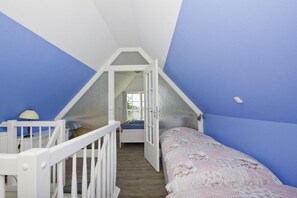 A bedroom with a sloped ceiling, a bed with a floral bedspread, a white crib, and a window with curtains. - A Seaside Getaway, Private Swimming Area - Gutshof Ostseeblick FeWo 01 - (Putbus)